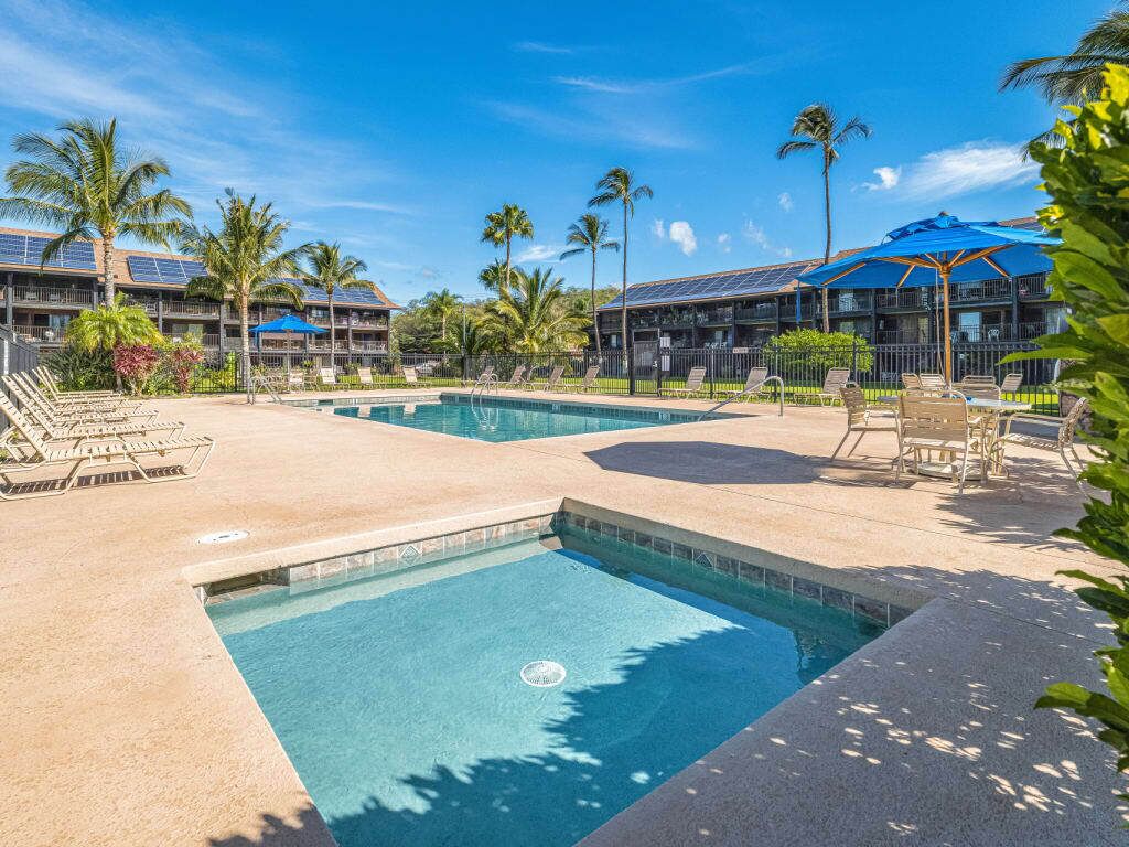 A pool area with lounge chairs, a pool, and a building with solar panels.