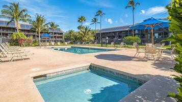 A pool area with lounge chairs, a pool, and a building with solar panels.