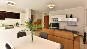 Un salon moderne comprenant un canapé, une table à manger avec des chaises, un téléviseur et un coin cuisine avec des placards et une cuisinière.