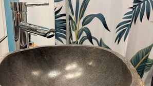 Un lavabo de piedra con un grifo moderno en un baño con cortina de ducha de temática tropical.