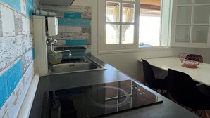 Una cocina con tope de inducción negro, un lavamanos y un ventanal con cortinas.