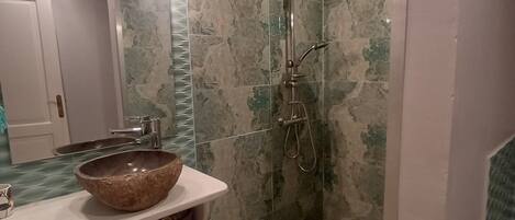 A bathroom with a stone sink, a shower, and a tiled floor.