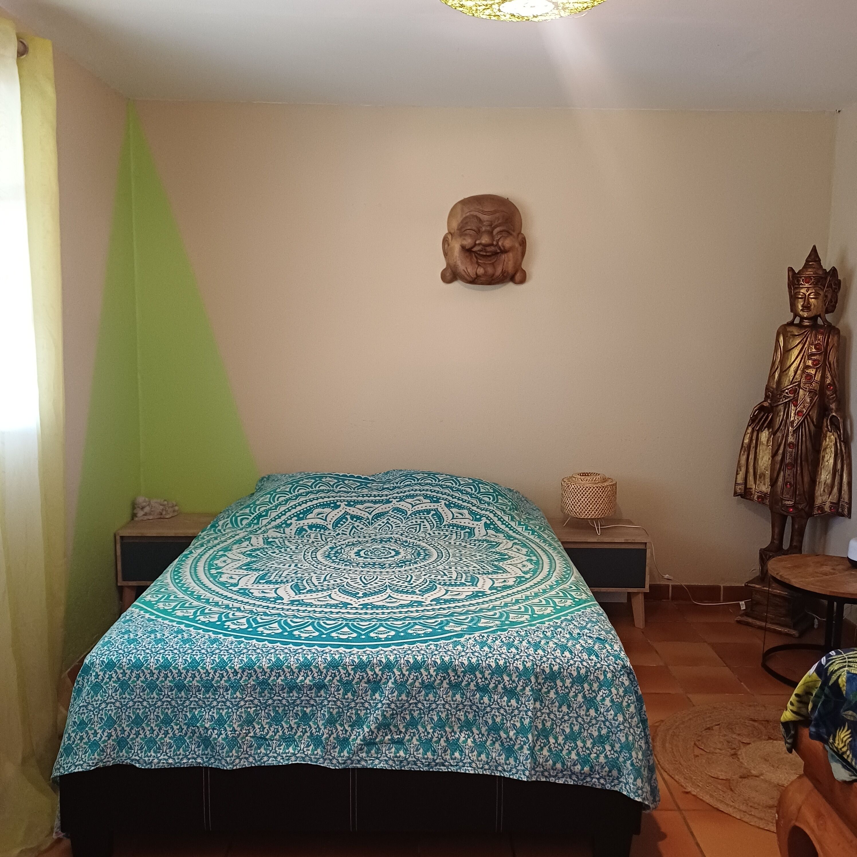 A room with a bed, a Buddha statue, a wall-mounted Buddha head, and a green wall.