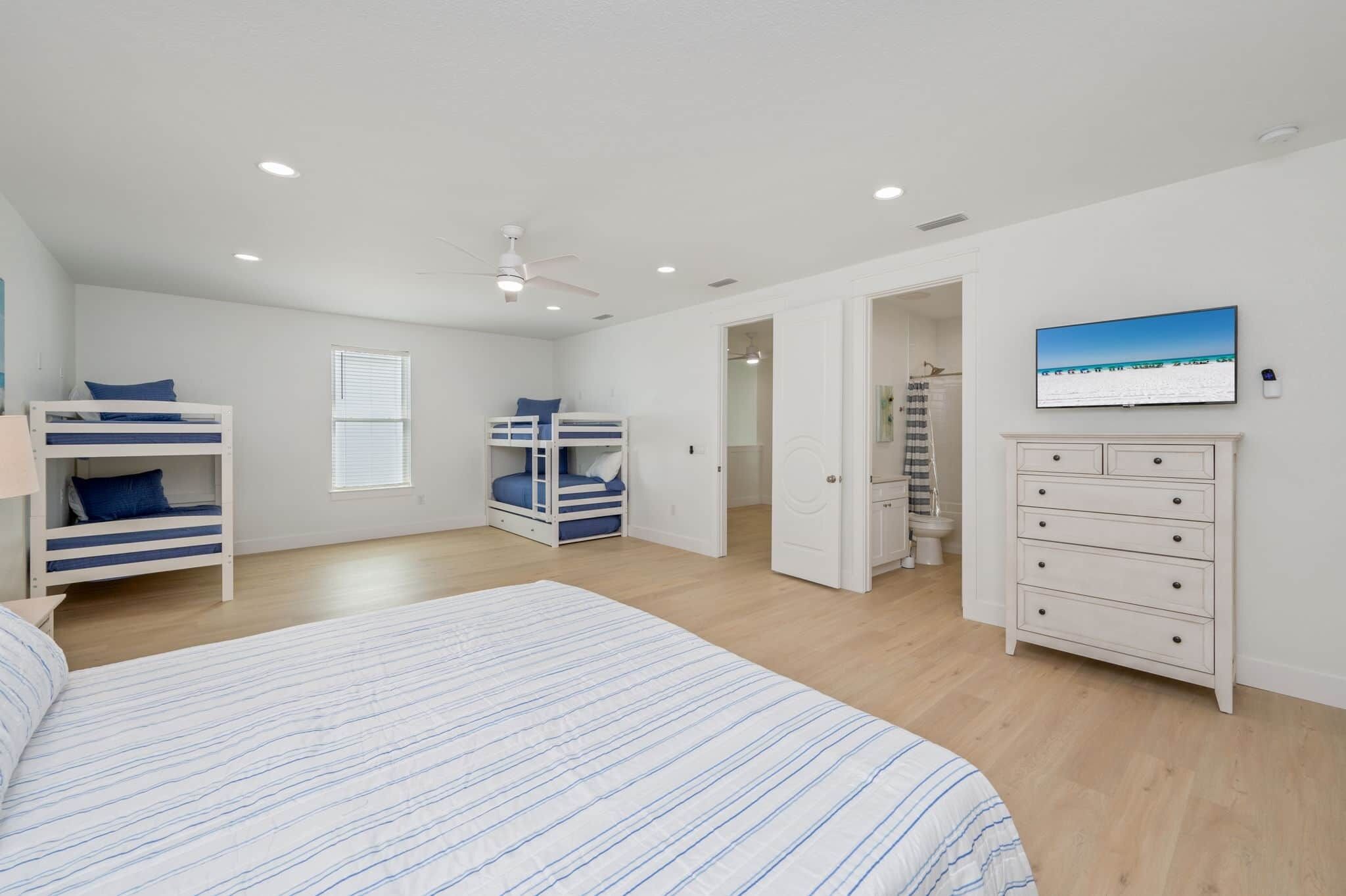 A bedroom with bunk beds, a bed, a dresser, a ceiling fan, and a painting on the wall.
