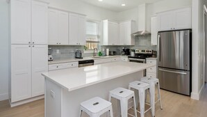 A modern kitchen with white cabinets, stainless steel appliances, and a central island with stools. - "Blue Pearl"| LUXURY HOME | PRIVATE POOL | SPA | 6 SEAT CART (Miramar Beach)