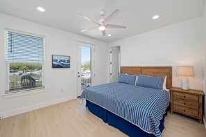 A bedroom with a bed, a ceiling fan, a nightstand, a lamp, a window with blinds, and a door. - "Blue Pearl"| LUXURY HOME | PRIVATE POOL | SPA | 6 SEAT CART (Miramar Beach)