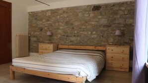 Une chambre avec un lit en bois, un mur en pierre, deux tables de chevet et un radiateur.