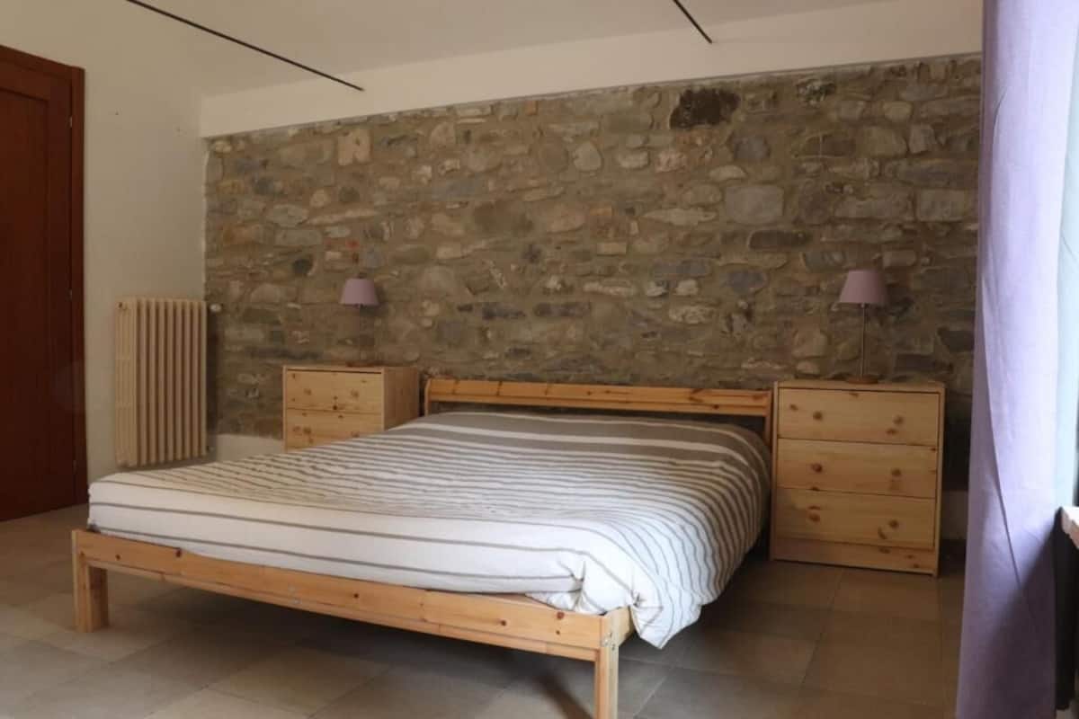 A bedroom with a wooden bed, stone wall, two nightstands, and a radiator.