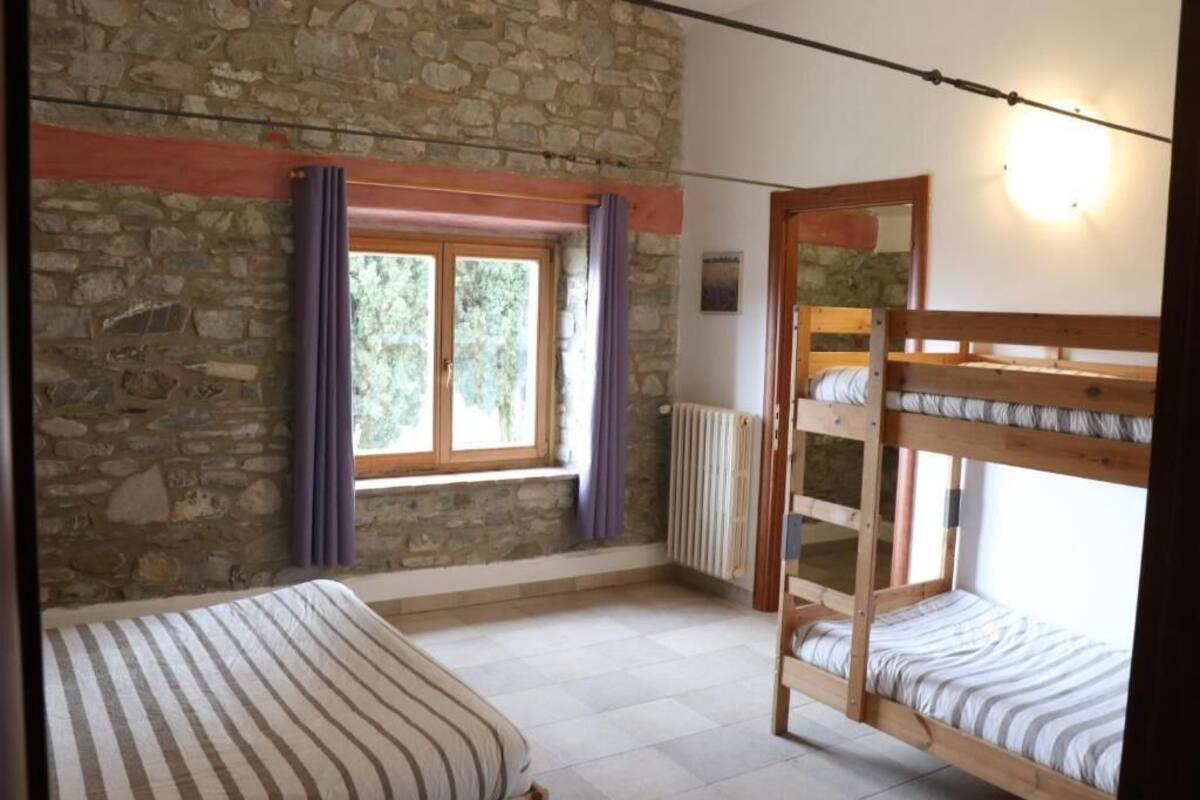 A room with a stone wall, a window with purple curtains, a bunk bed, and a single bed with striped bedding.
