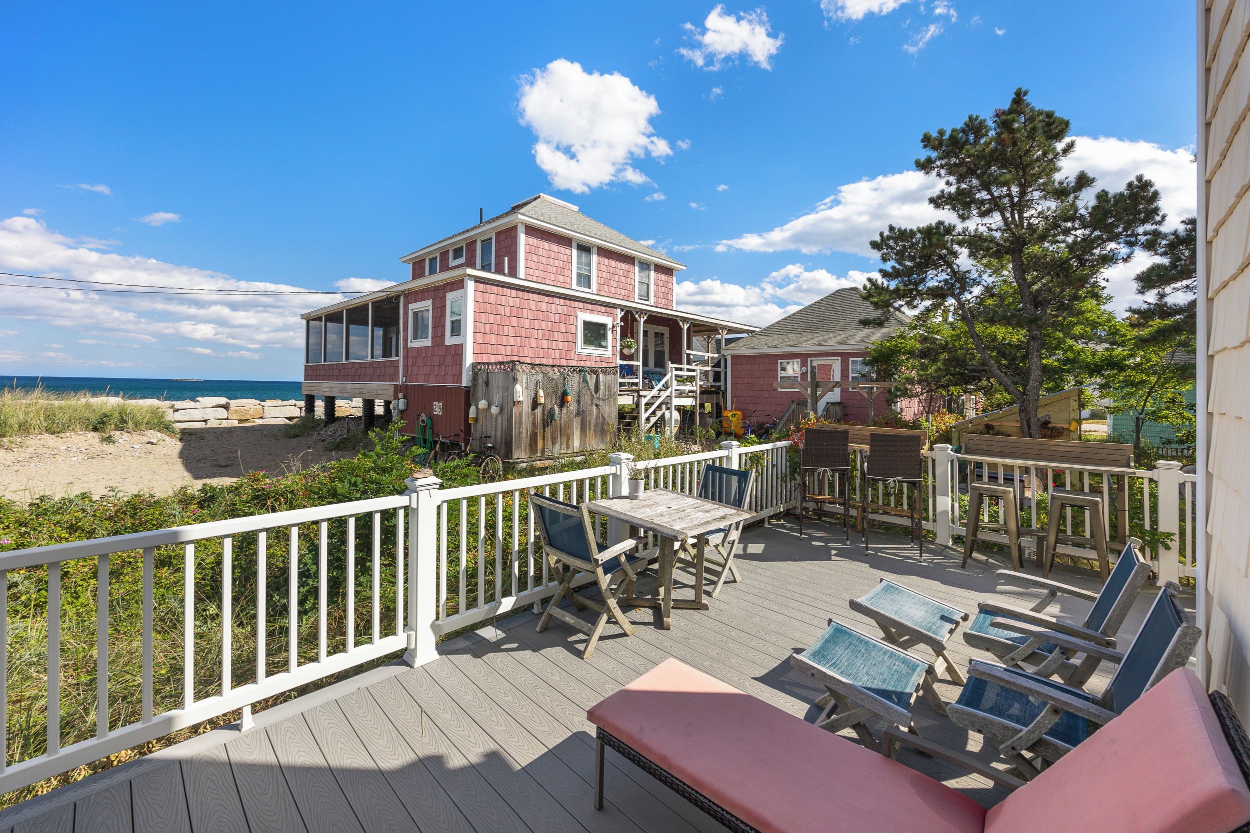 A beachfront property with a wooden deck, outdoor seating, and a view of the ocean.