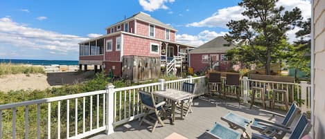 A beachfront property with a wooden deck, outdoor seating, and a view of the ocean.