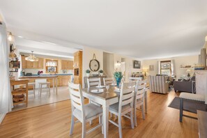 A spacious living area with a dining table set for four, a kitchen with wooden cabinets, and a cozy seating area with a sofa and armchairs.