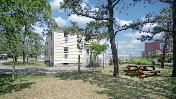 A two-story building with a white exterior, surrounded by trees and a picnic table in a grassy area.
