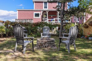 A two-story house with a red exterior and a porch. There are two Adirondack chairs and a stone fire pit in the front yard.