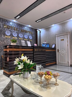 A hotel reception desk with clocks displaying different cities, a reception sign, a reception area, and a door labeled 'WC'. - AFSONA HOTEL (Bukhara)