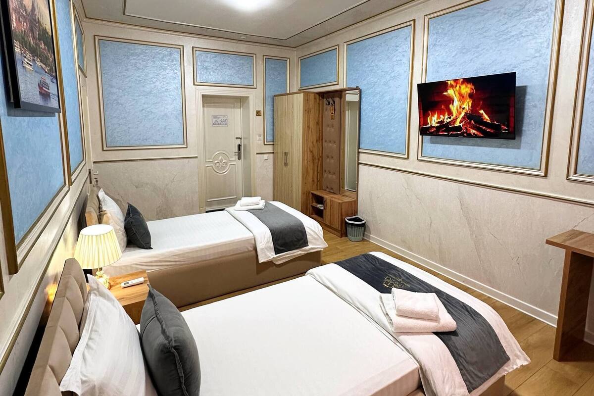 Habitación de hotel con dos camas, televisión, armario de madera, una mesita con lámpara y una puerta.