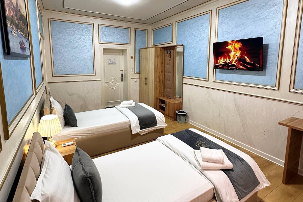 Habitación de hotel con dos camas, televisión, armario de madera, una mesita con lámpara y una puerta.