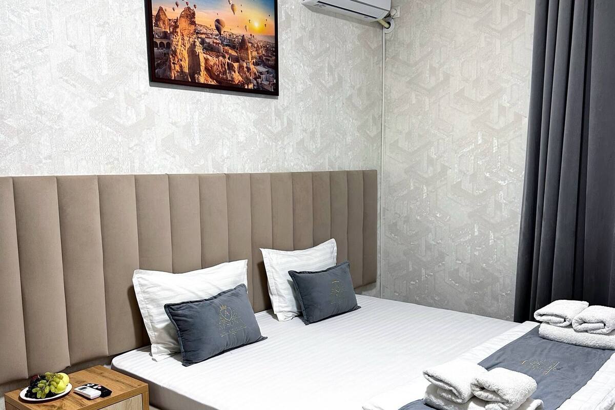 Habitación de hotel con cama, mesita de noche, aire acondicionado instalado en la pared y una pintura con vista a la ciudad.