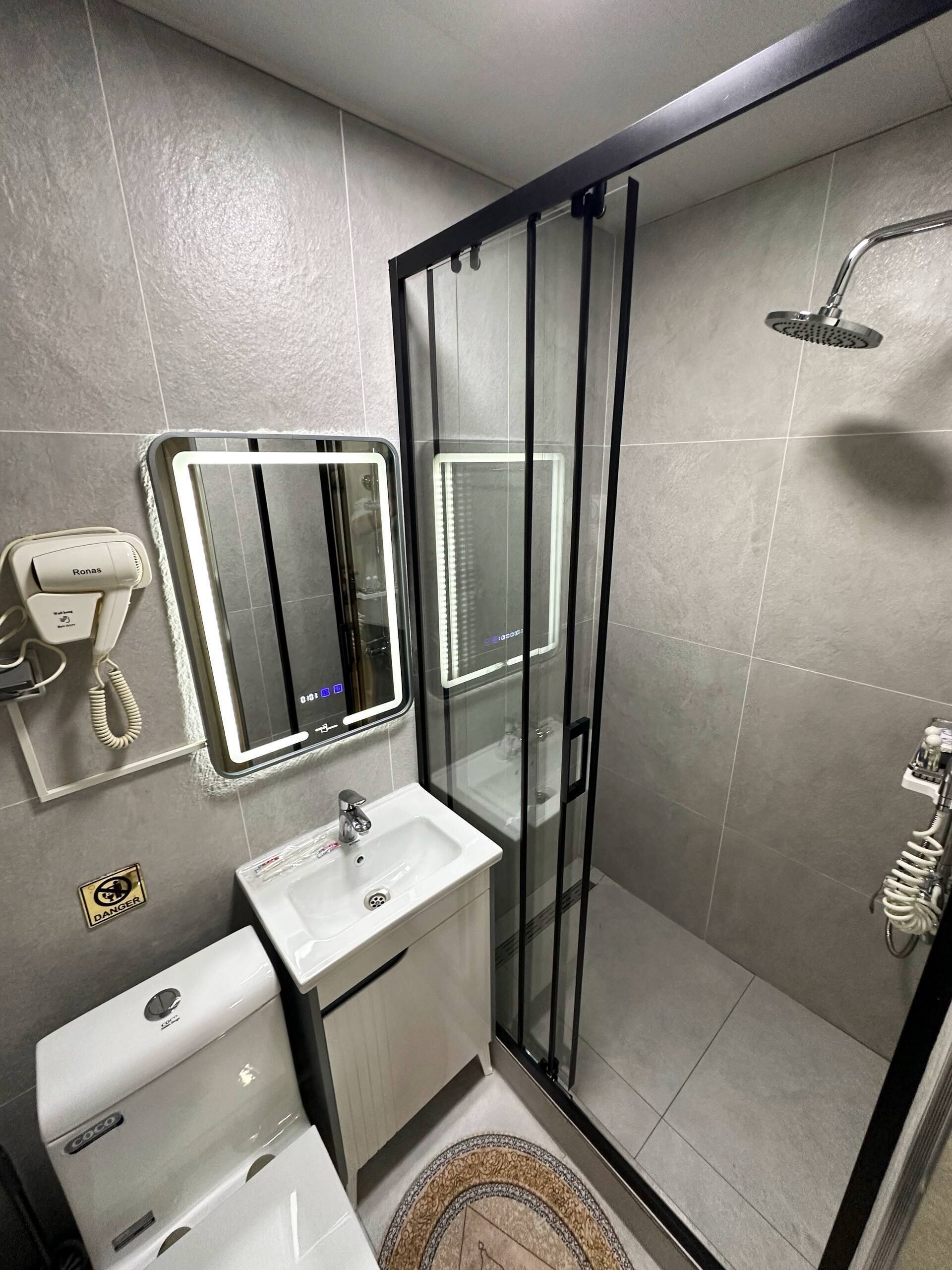 Un baño moderno con ducha de vidrio, lavamanos con tocador y espejo con iluminación integrada.