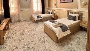 A hotel room with two beds, a television, a desk, and a chandelier. - AFSONA HOTEL (Bukhara)