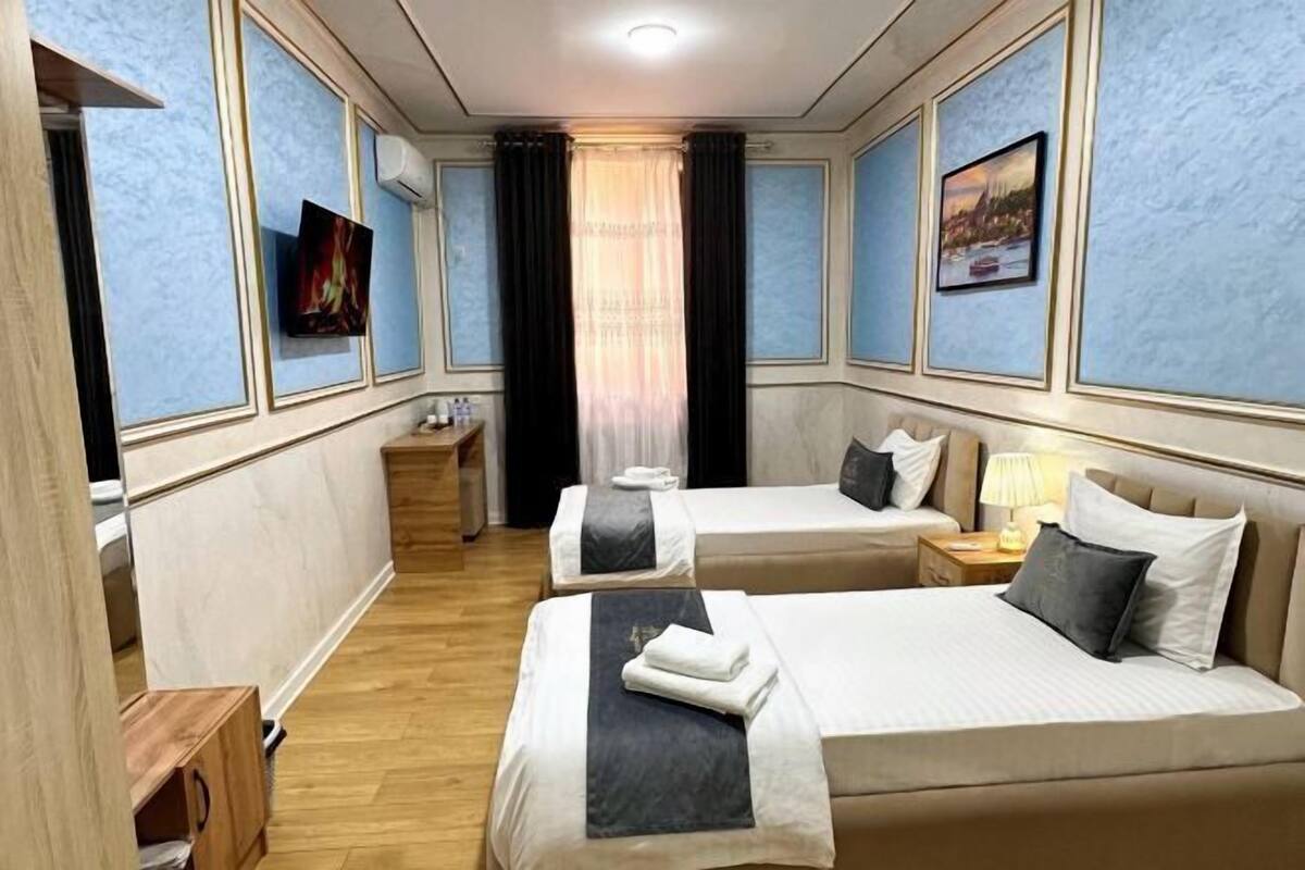 Una habitación de hotel con dos camas, un televisor, una mesita de noche y una ventana con cortinas.