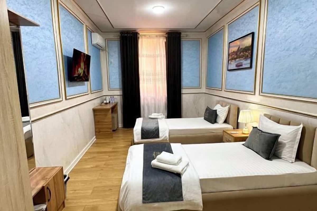 A hotel room with two beds, a TV, a nightstand, and a window with curtains.