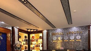 A hotel reception area with a marble floor, sofas, a reception desk, and a wall displaying clocks set to different cities. - AFSONA HOTEL (Bukhara)