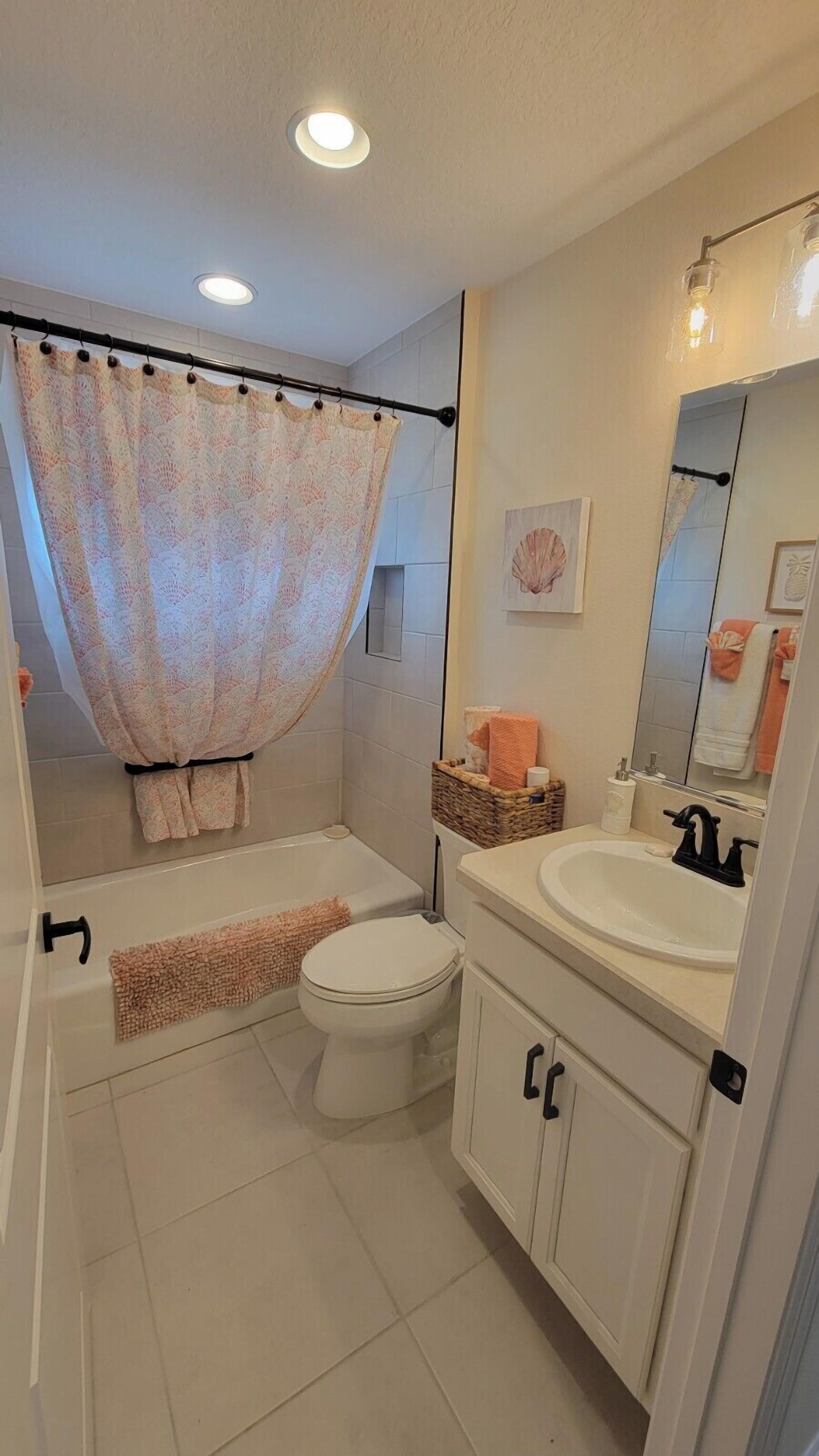 A bathroom with a shower curtain, a toilet, a sink, and a mirror.