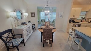 A modern kitchen with white cabinets, a dining area with a round table and chairs, and a small island with a sink. - After Dune Delight - 3/2 w/ Golf Cart in The Village of Cason Hammock (Cason Hammock, The Villages)