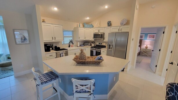A modern kitchen with white cabinets, a central island, and a dining area with two chairs. - After Dune Delight - 3/2 w/ Golf Cart in The Village of Cason Hammock (Cason Hammock, The Villages)