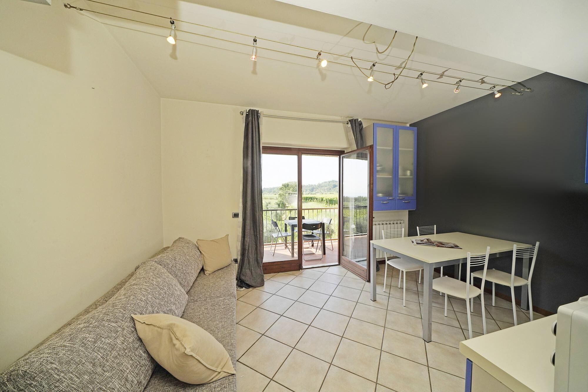 Un salon avec un canapé, une table à manger avec des chaises, un balcon avec vue et un coin cuisine avec des placards.