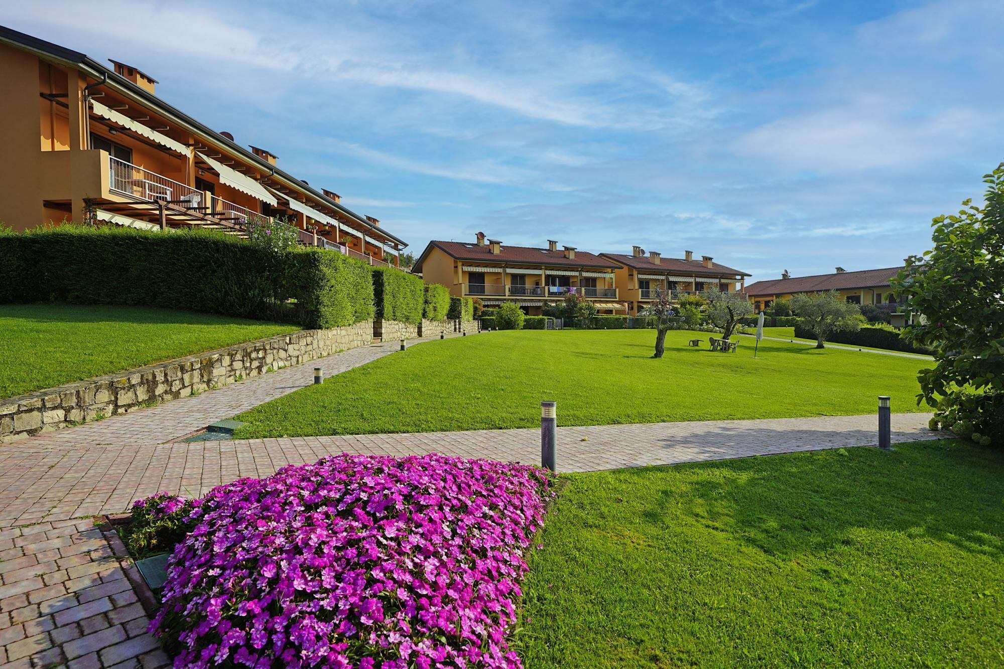 A residential complex with multiple two-story buildings, a paved walkway, and a well-maintained lawn.