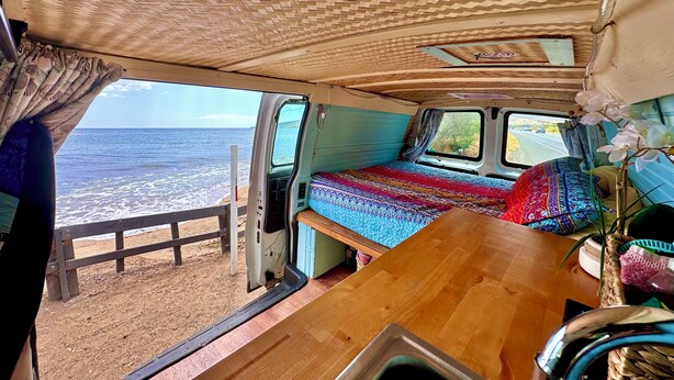 A van with a bed, a window, and a view of the ocean. - Deluxe Camper Van  with Aloha (Kihei)