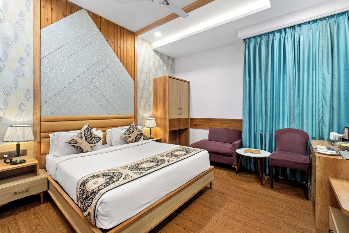Una habitación de hotel moderna con una cama grande, cabecera de madera, un escritorio con silla y una cortina azul.