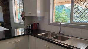 A kitchen with white cabinets, a black countertop, a stainless steel sink, and a red kettle.