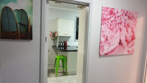 A kitchen with white cabinets, a green stool, and a pink floral painting on the wall.