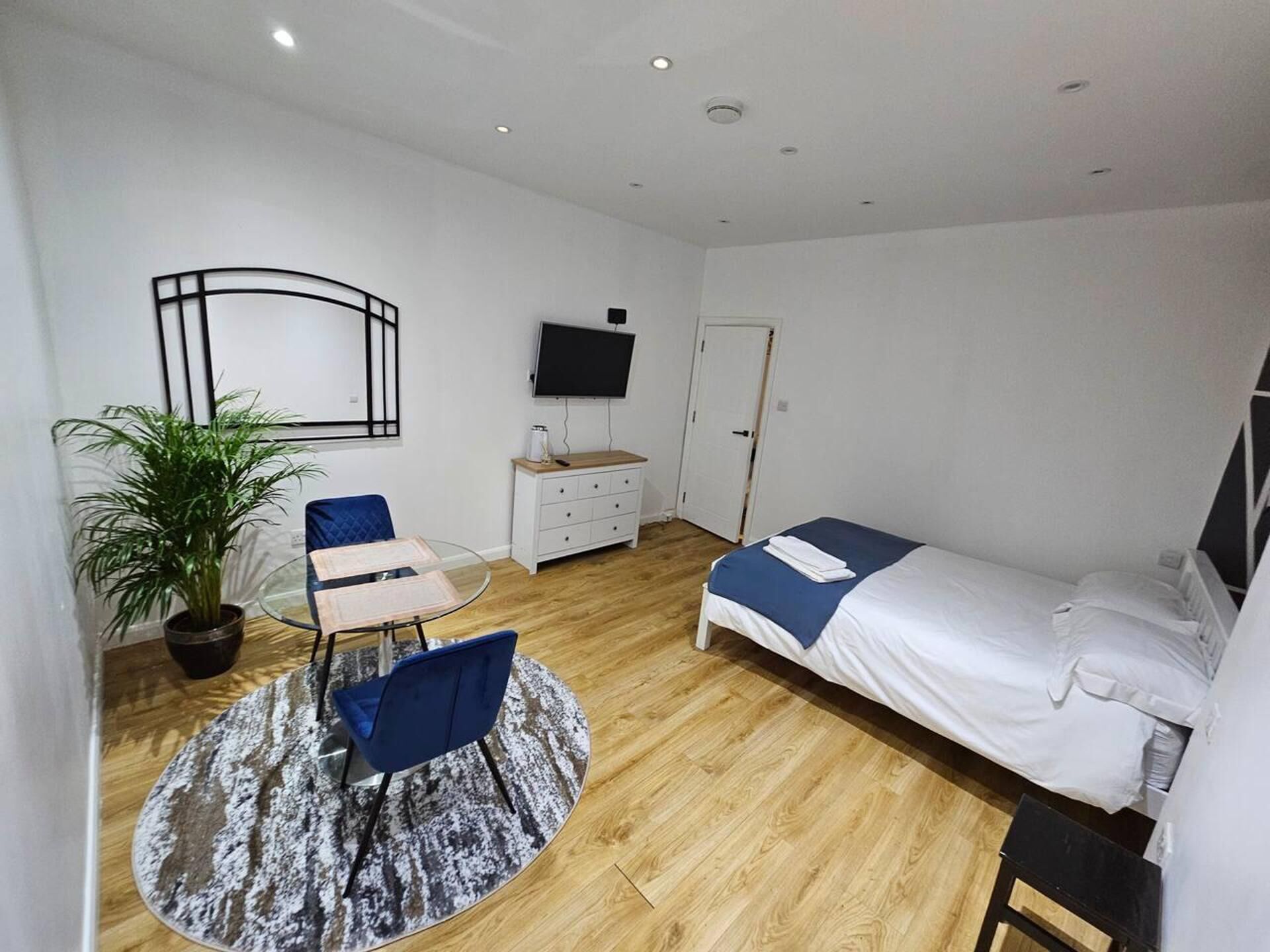 Una habitación pequeña y ordenada con cama, escritorio, silla, planta en maceta y televisor.