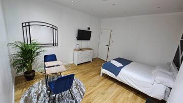 Una habitación pequeña y ordenada con cama, escritorio, silla, planta en maceta y televisor.