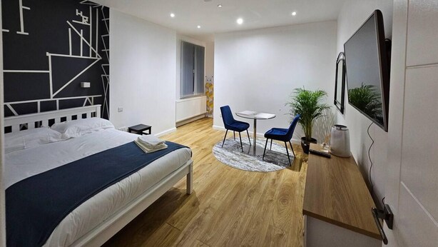 Un dormitorio moderno con una cama, un escritorio, dos sillas, un televisor y una ventana.