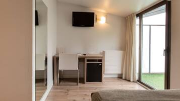 Una habitación de hotel con cama, escritorio con silla, televisor montado en la pared y puerta corrediza de vidrio al exterior.