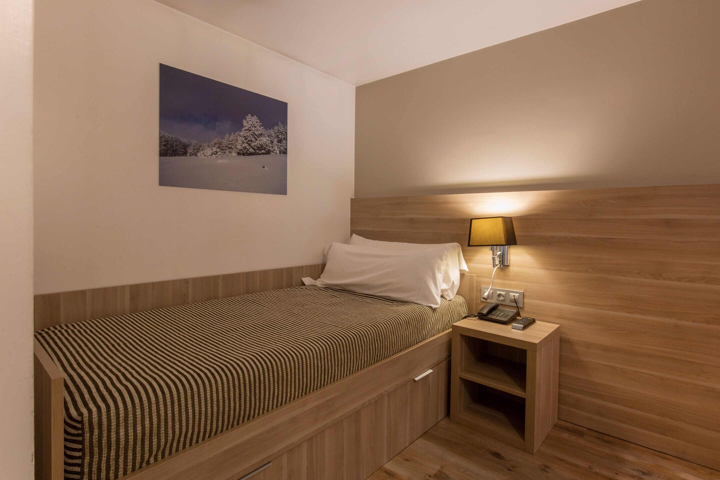 Un dormitorio pequeño y ordenado con una cama individual, una mesita de noche con lámpara y un cuadro enmarcado en la pared.