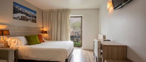 A hotel room with a bed, bedside lamps, a TV, a desk, and a view of the outdoors.