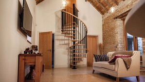 Amplia sala de estar con una escalera de madera, un sofá blanco y un televisor instalado en la pared.