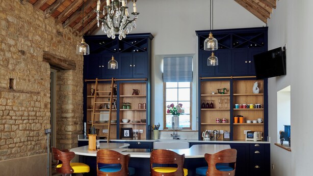 Una cocina rústica con pared de piedra, vigas de madera y una isla grande con taburetes de bar.