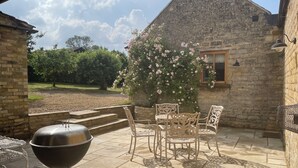 Un patio con una parrilla, mobiliario exterior y un edificio de piedra con una ventana.
