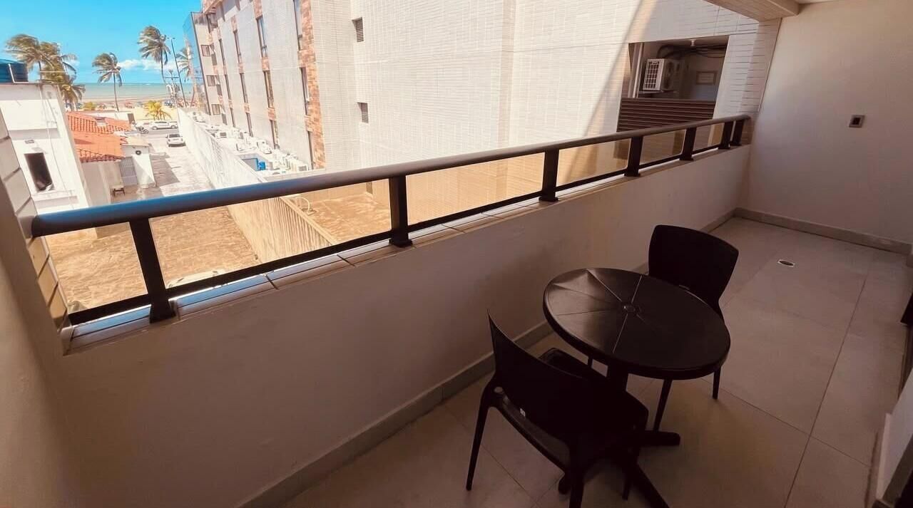 Un balcón con mesa y sillas, con vistas a una playa y edificios.