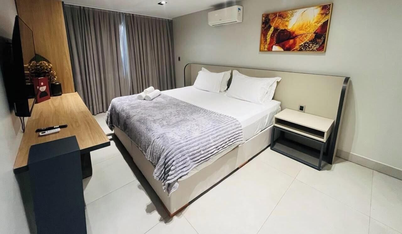 Quarto de hotel com cama, mesa de cabeceira e escrivaninha com cadeira.