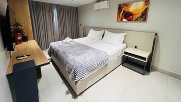Quarto de hotel com cama, mesa de cabeceira e escrivaninha com cadeira.