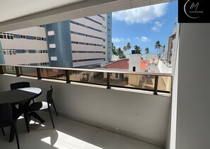 Un balcón con mesa y sillas, vistas a edificios y cielo despejado.