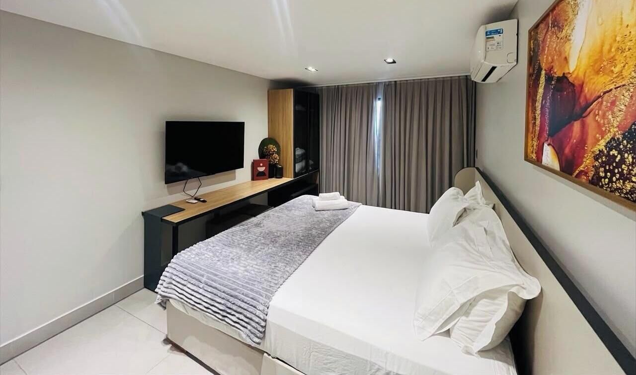 A modern hotel room with a bed, a flat-screen TV, a desk, and a large painting on the wall.